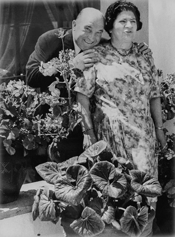 Una pareja posa sentada junto a un gran arreglo de flores.