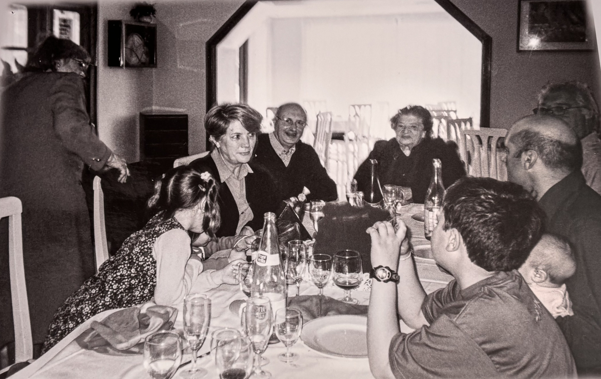 Varias personas se sientan alrededor de una mesa con copas en un comedor con retratos en la pared.