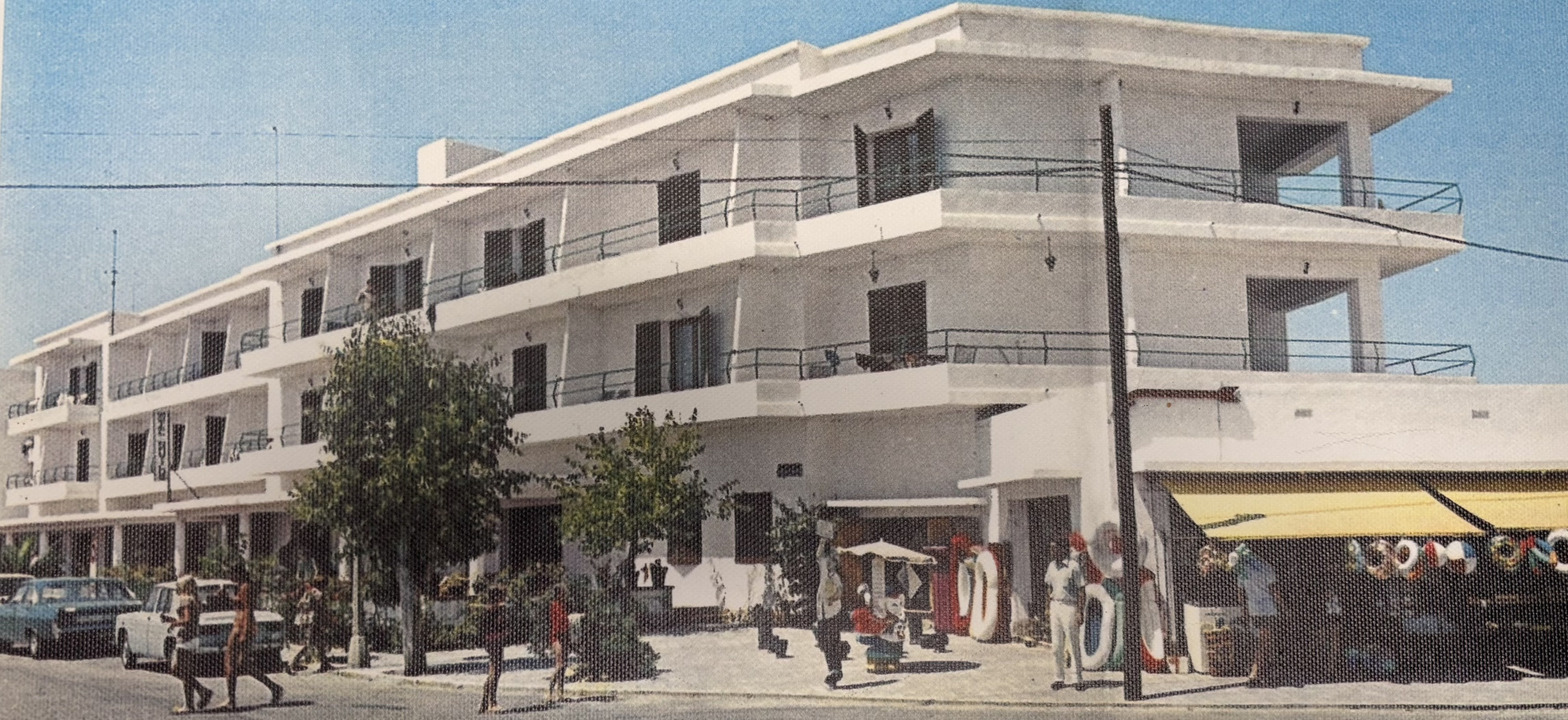 Se ve la fachada de un edificio con balcones y una terraza con toldo amarillo.